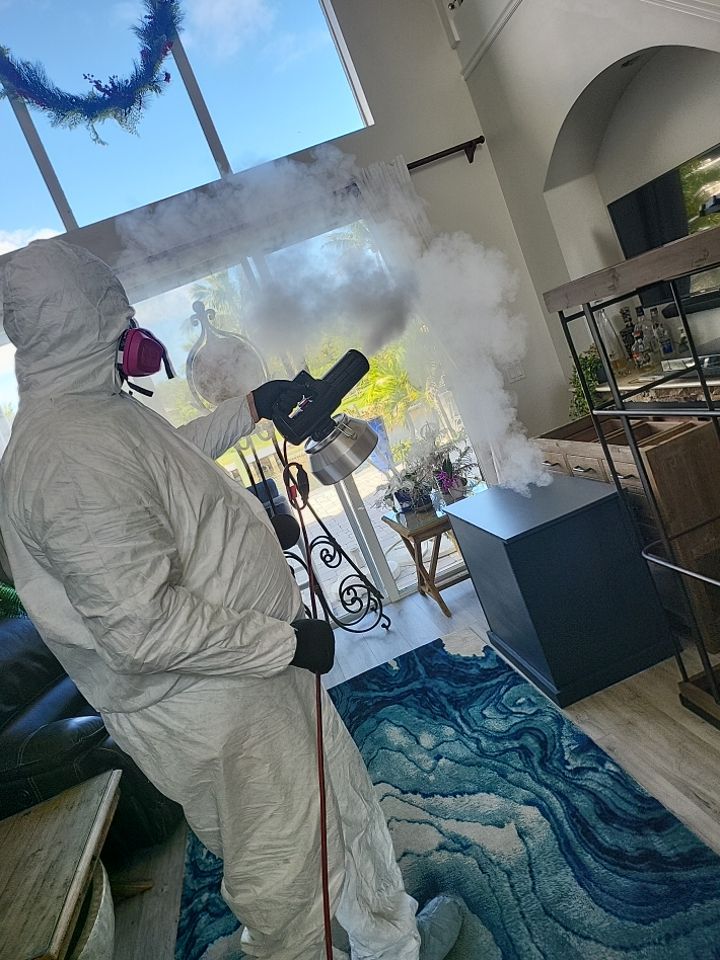 Technician in full PPE thermal fogging large open living room with pool view